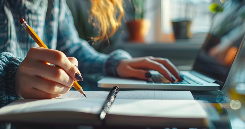 Persona frente a un ordenador escribiendo en un cuaderno