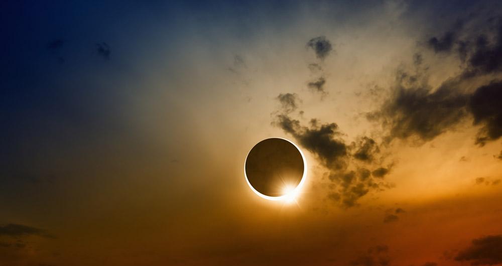 Eclipse solar total con anillo luminoso visible entre nubes al atardecer.